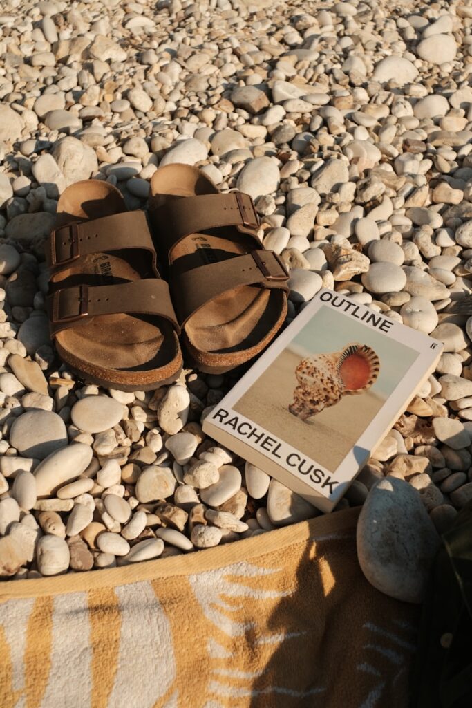 Brown sandals and book on a pebble beach.